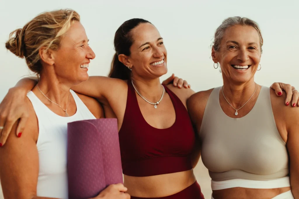 Tre donne sorridenti in abbigliamento da yoga che si abbracciano