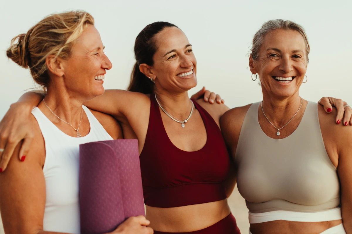 Tre donne sorridenti in abbigliamento da yoga che si abbracciano